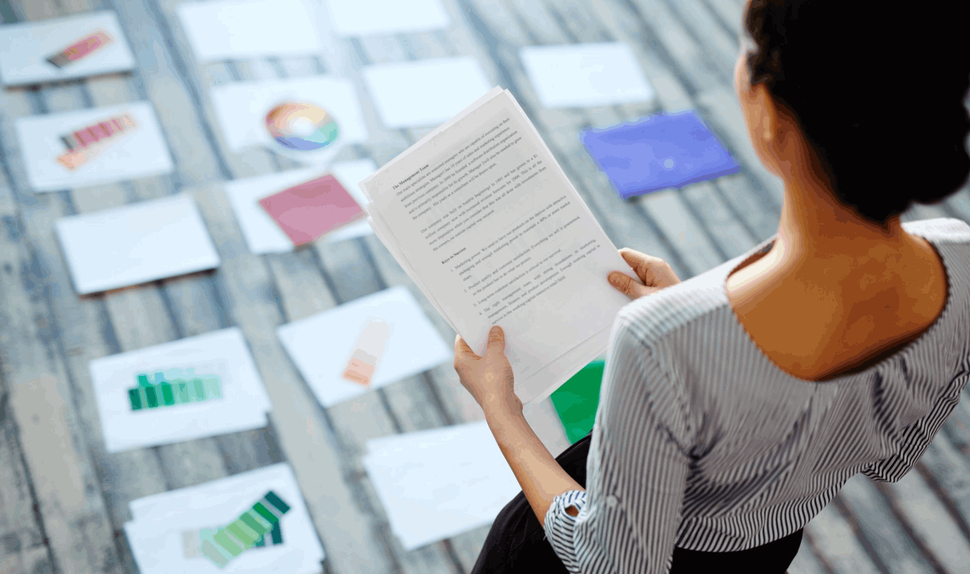 Person reviewing printed documents while examining colour samples spread on the floor, showcases White Paper: Research-Backed Insight.